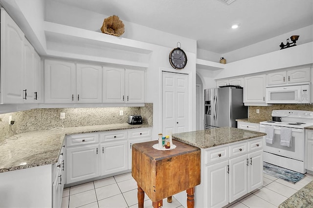 kitchen with white cabinets, light tile patterned floors, light stone countertops, and white appliances