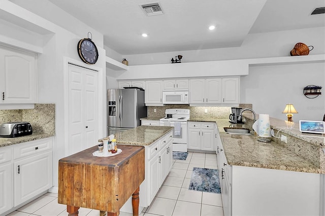 kitchen featuring visible vents, a peninsula, white appliances, a sink, and light stone counters