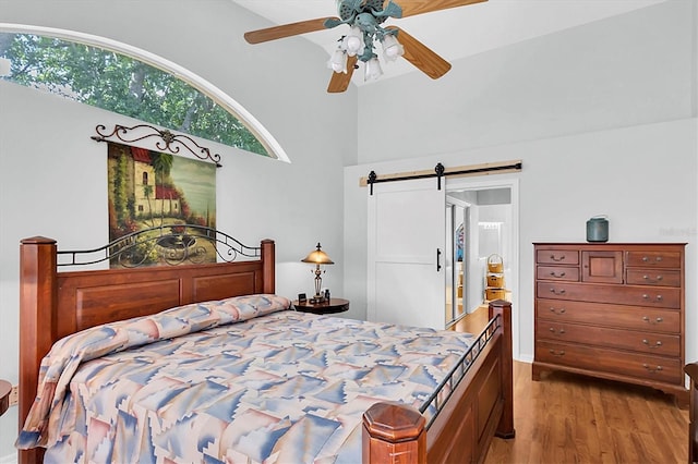 bedroom with a barn door, ceiling fan, and wood finished floors