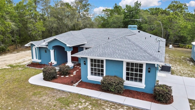 ranch-style home with roof with shingles, stucco siding, and central air condition unit