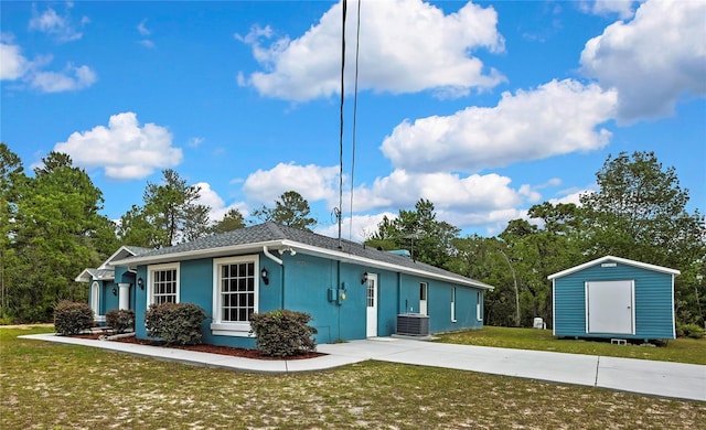 view of front of property with a shed, central air condition unit, stucco siding, an outdoor structure, and a front lawn