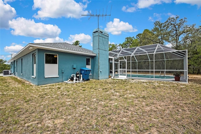 rear view of house with central AC unit, a yard, an outdoor pool, a chimney, and a lanai