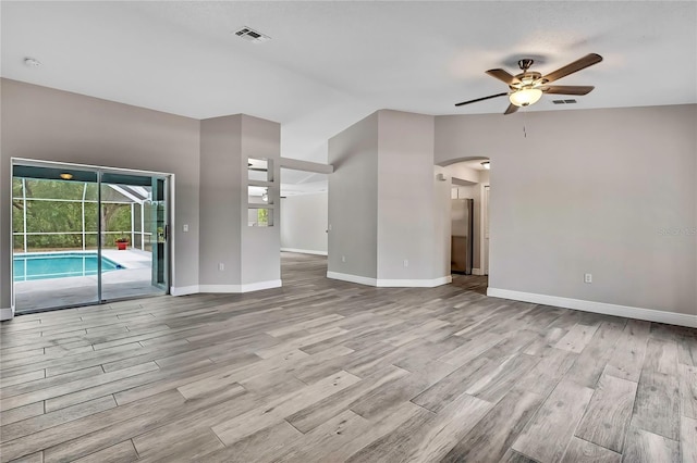 unfurnished living room featuring a ceiling fan, wood finished floors, arched walkways, and baseboards