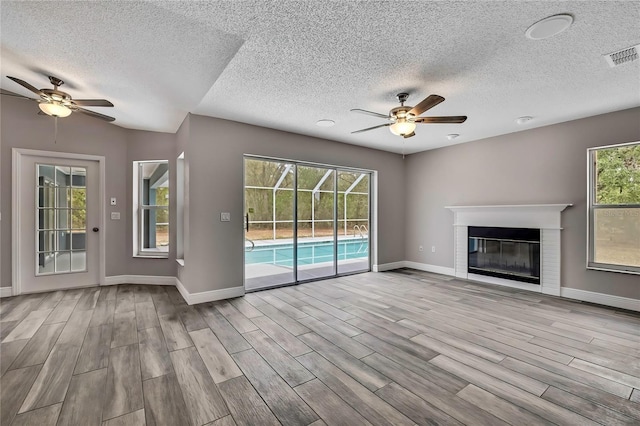 unfurnished living room with ceiling fan, wood finished floors, baseboards, and a textured ceiling