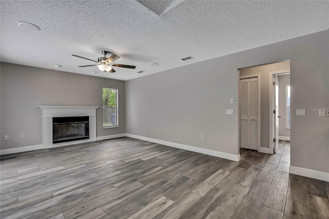 unfurnished living room with a ceiling fan, wood finished floors, a textured ceiling, a fireplace with flush hearth, and baseboards