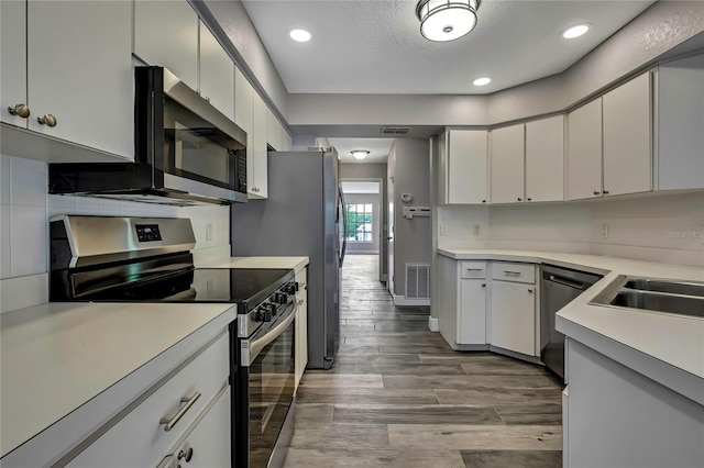 kitchen featuring stainless steel appliances, wood finished floors, light countertops, a sink, and recessed lighting