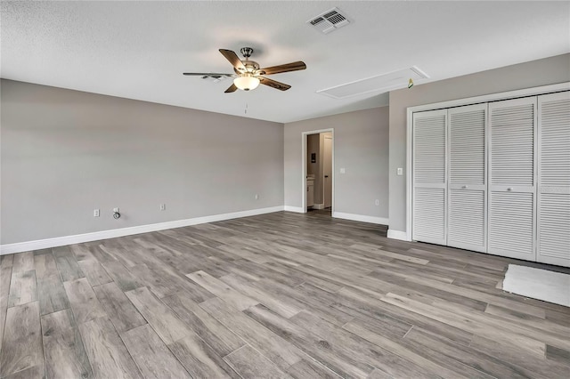 unfurnished bedroom featuring attic access, wood finished floors, baseboards, and a closet