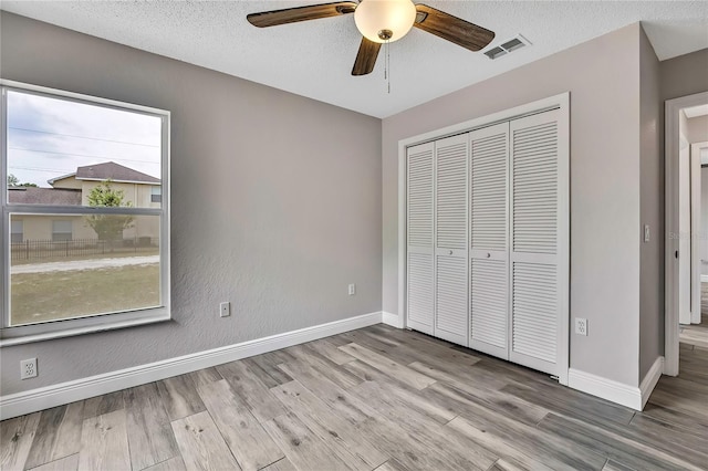 unfurnished bedroom with wood finished floors, baseboards, a closet, a textured ceiling, and a ceiling fan