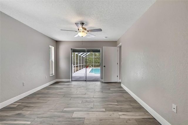 empty room with ceiling fan, a textured ceiling, wood finished floors, baseboards, and a textured wall