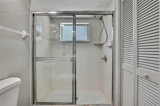 bathroom featuring a textured wall, a closet, toilet, and a shower stall