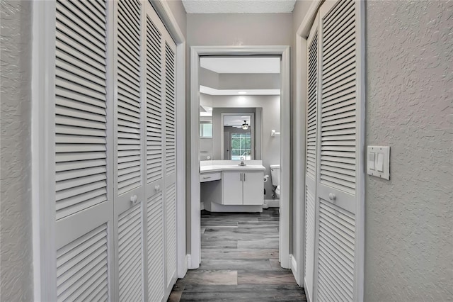 hall with a textured wall, dark wood finished floors, and a sink