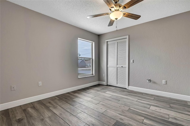 empty room with ceiling fan, a textured ceiling, wood finished floors, and baseboards