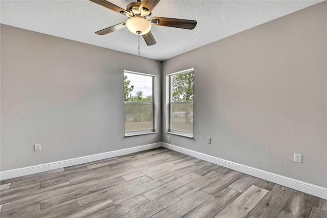 spare room with a textured ceiling, baseboards, wood finished floors, and a ceiling fan
