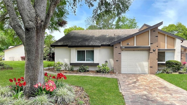 view of front of property with stucco siding, roof with shingles, a front yard, brick siding, and a garage