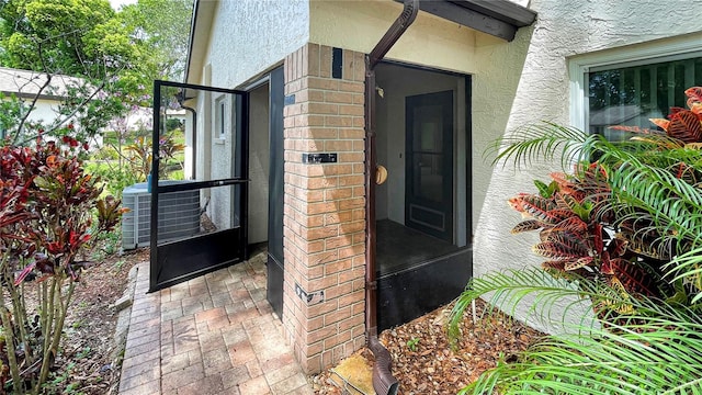 doorway to property with central air condition unit, stucco siding, and brick siding