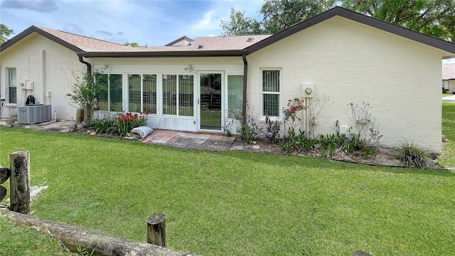 back of house featuring central AC, stucco siding, and a yard