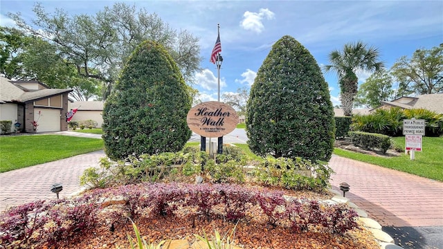 community sign featuring a lawn and decorative driveway
