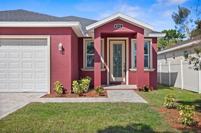 entrance to property with stucco siding, a garage, fence, and a lawn