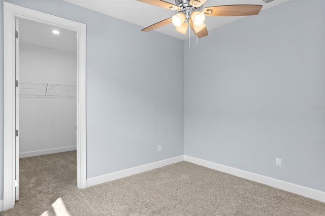 unfurnished bedroom featuring a closet, a spacious closet, baseboards, ceiling fan, and carpet