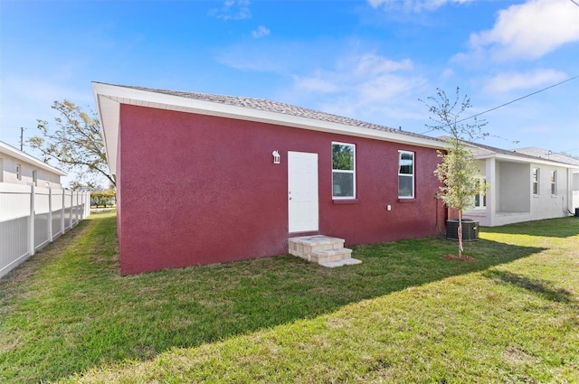 back of house with stucco siding, fence, cooling unit, and a yard