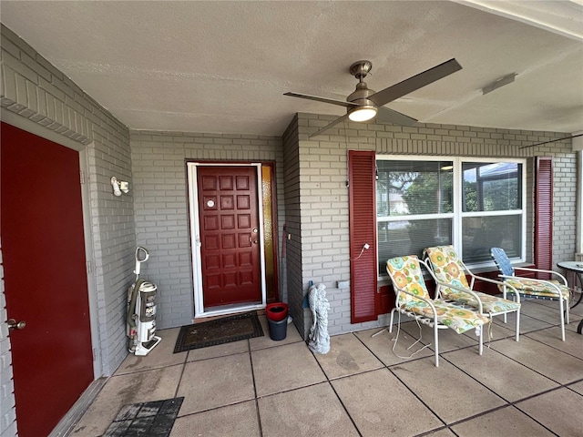 entrance to property with brick siding, a porch, and a ceiling fan