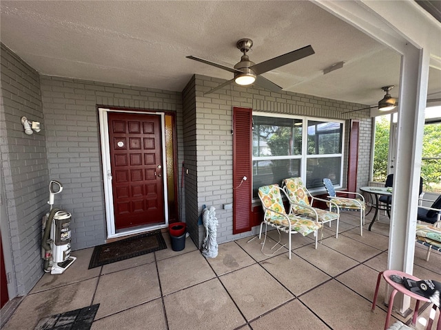 view of exterior entry with covered porch, brick siding, and a ceiling fan