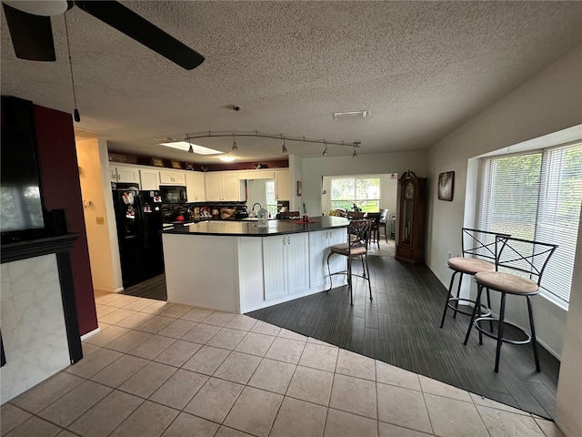 kitchen with white cabinetry, tile patterned floors, a sink, dark countertops, and black appliances
