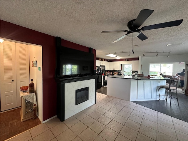 kitchen with white cabinetry, a textured ceiling, light tile patterned flooring, dark countertops, and a ceiling fan
