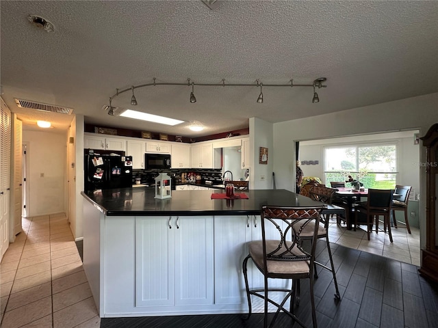 kitchen with decorative backsplash, white cabinets, visible vents, dark countertops, and black appliances