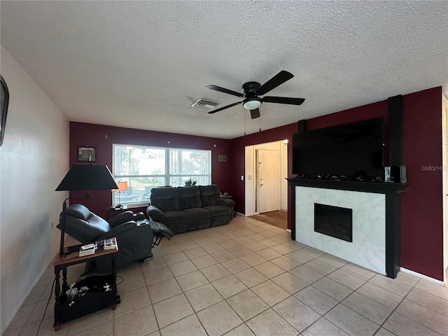 living room featuring a textured ceiling, visible vents, a fireplace, ceiling fan, and light tile patterned floors