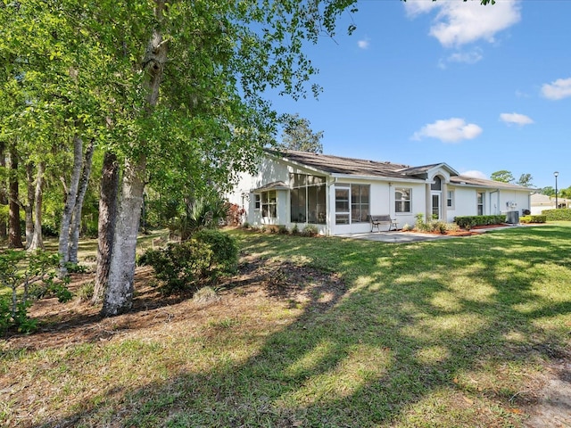 rear view of house with a lawn, a sunroom, stucco siding, and a patio area