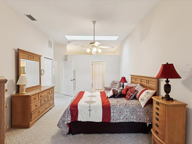 bedroom with light colored carpet, visible vents, vaulted ceiling with skylight, and ceiling fan