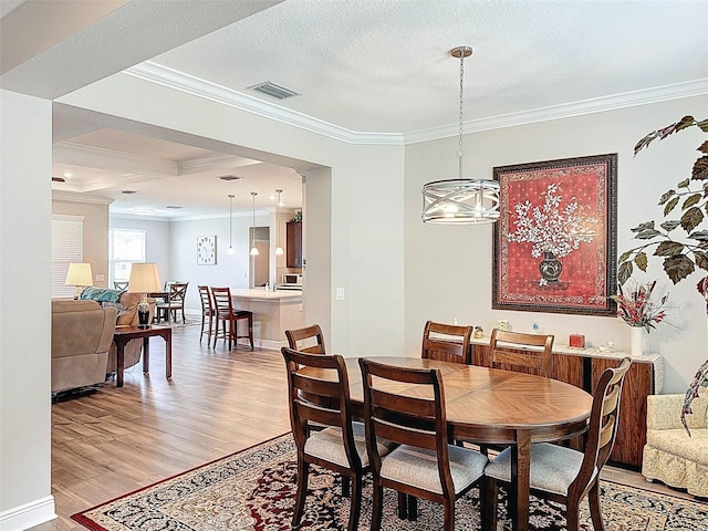dining room featuring a textured ceiling, light wood-type flooring, baseboards, visible vents, and ornamental molding