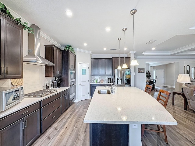 kitchen featuring dark brown cabinetry, a sink, light wood-type flooring, stainless steel appliances, and wall chimney range hood