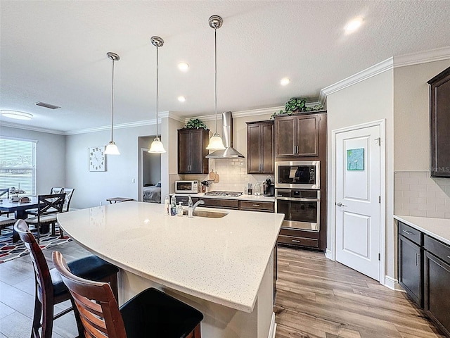 kitchen featuring wall chimney range hood, a sink, appliances with stainless steel finishes, and a kitchen breakfast bar