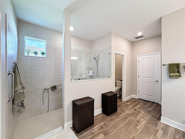 full bath with toilet, a walk in shower, wood finished floors, baseboards, and visible vents