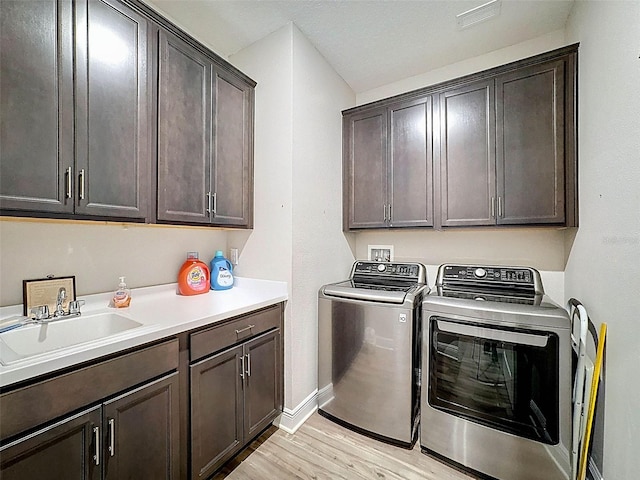 washroom featuring a sink, light wood-style flooring, baseboards, independent washer and dryer, and cabinet space