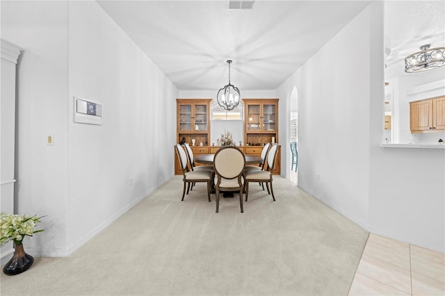 dining room featuring visible vents, a notable chandelier, arched walkways, light tile patterned floors, and light colored carpet