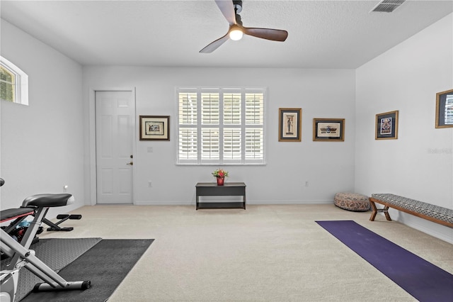 exercise area featuring a textured ceiling, visible vents, baseboards, a ceiling fan, and carpet floors