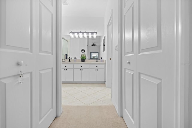 hall featuring light tile patterned flooring, a sink, and light carpet
