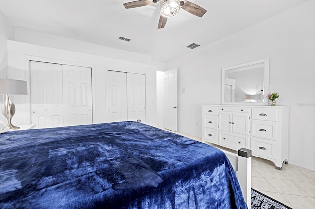 bedroom with light tile patterned floors, ceiling fan, visible vents, and two closets