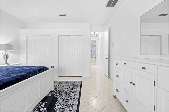 bedroom with two closets, light tile patterned floors, and visible vents