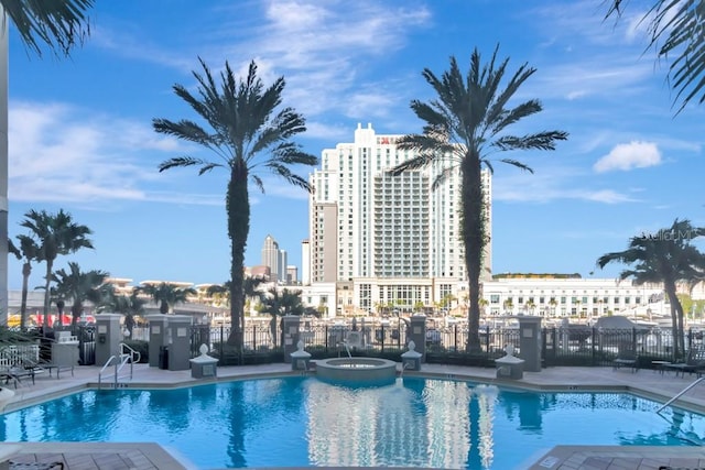 view of pool with a city view, a patio area, a pool with connected hot tub, and fence