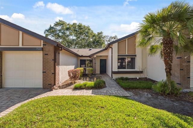 mid-century modern home featuring a garage, stucco siding, brick siding, a front lawn, and driveway