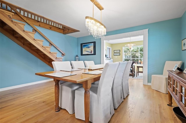 dining room with baseboards, light wood finished floors, an inviting chandelier, and stairway