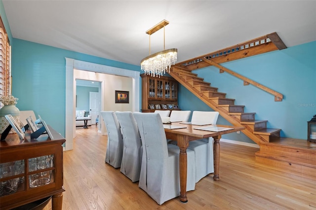 dining area with baseboards, light wood finished floors, a chandelier, and stairs