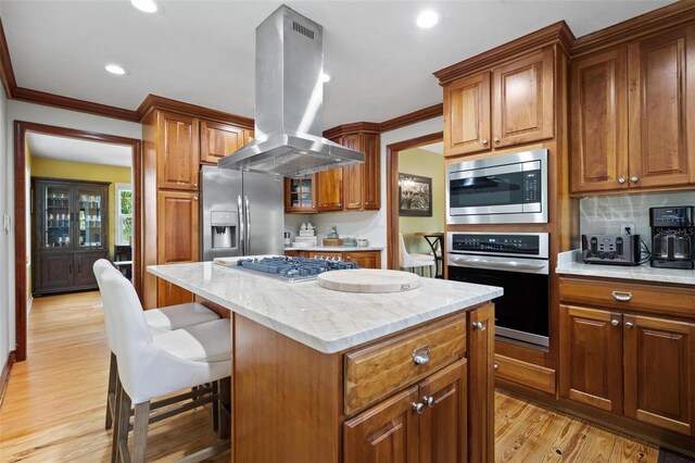 kitchen with brown cabinetry, stainless steel appliances, island range hood, light wood-style flooring, and a kitchen island