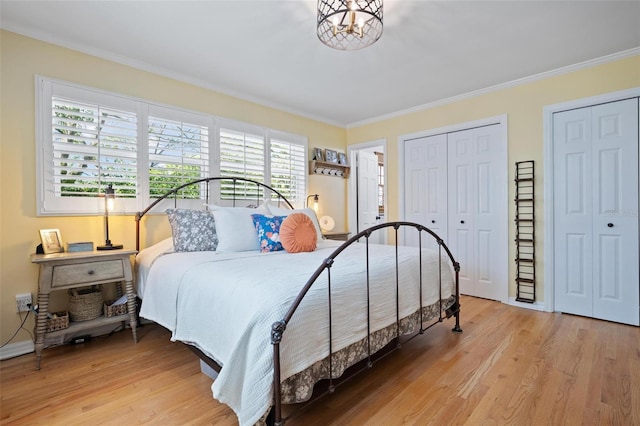 bedroom featuring light wood-type flooring, baseboards, ornamental molding, and multiple closets