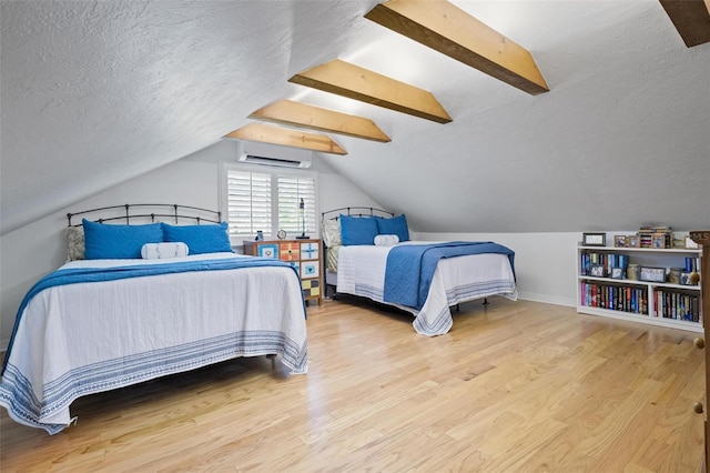 bedroom with baseboards, a wall mounted air conditioner, light wood-style flooring, a textured ceiling, and vaulted ceiling with beams