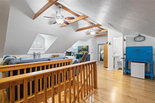 bedroom featuring light wood-style flooring, a textured ceiling, a ceiling fan, a sink, and vaulted ceiling with beams